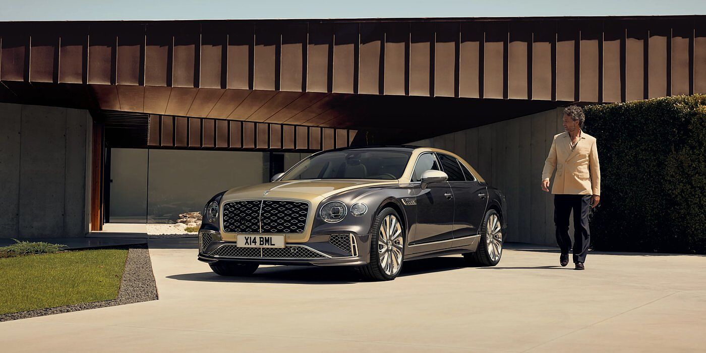 Bentley Ho Chi Minh Bentley New Flying Spur Mulliner V8 hybrid sedan front three quarters in Rose Gold over Magnetic paint, parked near modern home