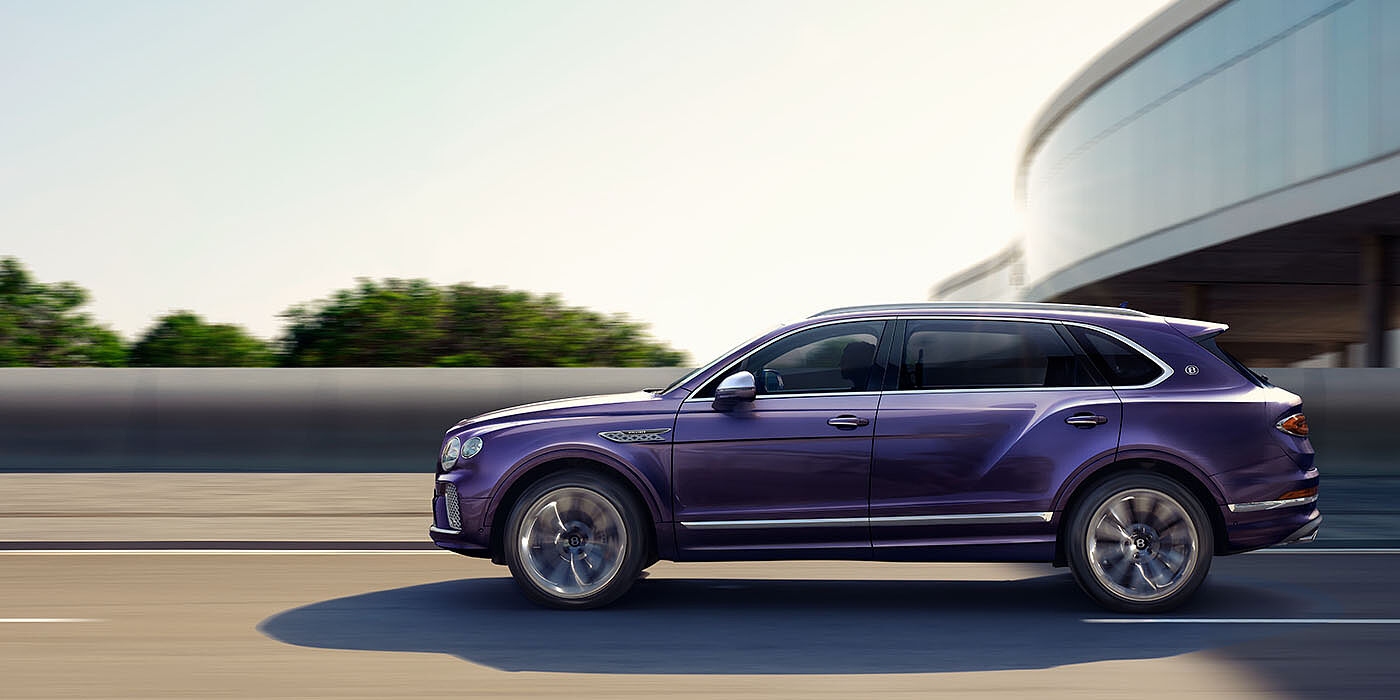 Bentley Ho Chi Minh Bentley Bentayga Extended Wheelbase Mulliner luxury SUV profile in Tanzanite Purple paint, driving on an country road past trees.