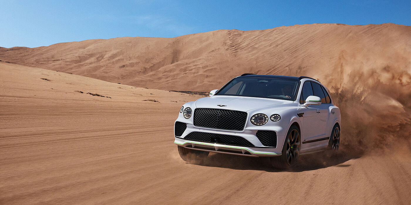 Bentley Ho Chi Minh Bentley Bentayga Speed SUV front three quarter in Snow Quarts Pearlescent by Mulliner white paint driving dynamically through the desert