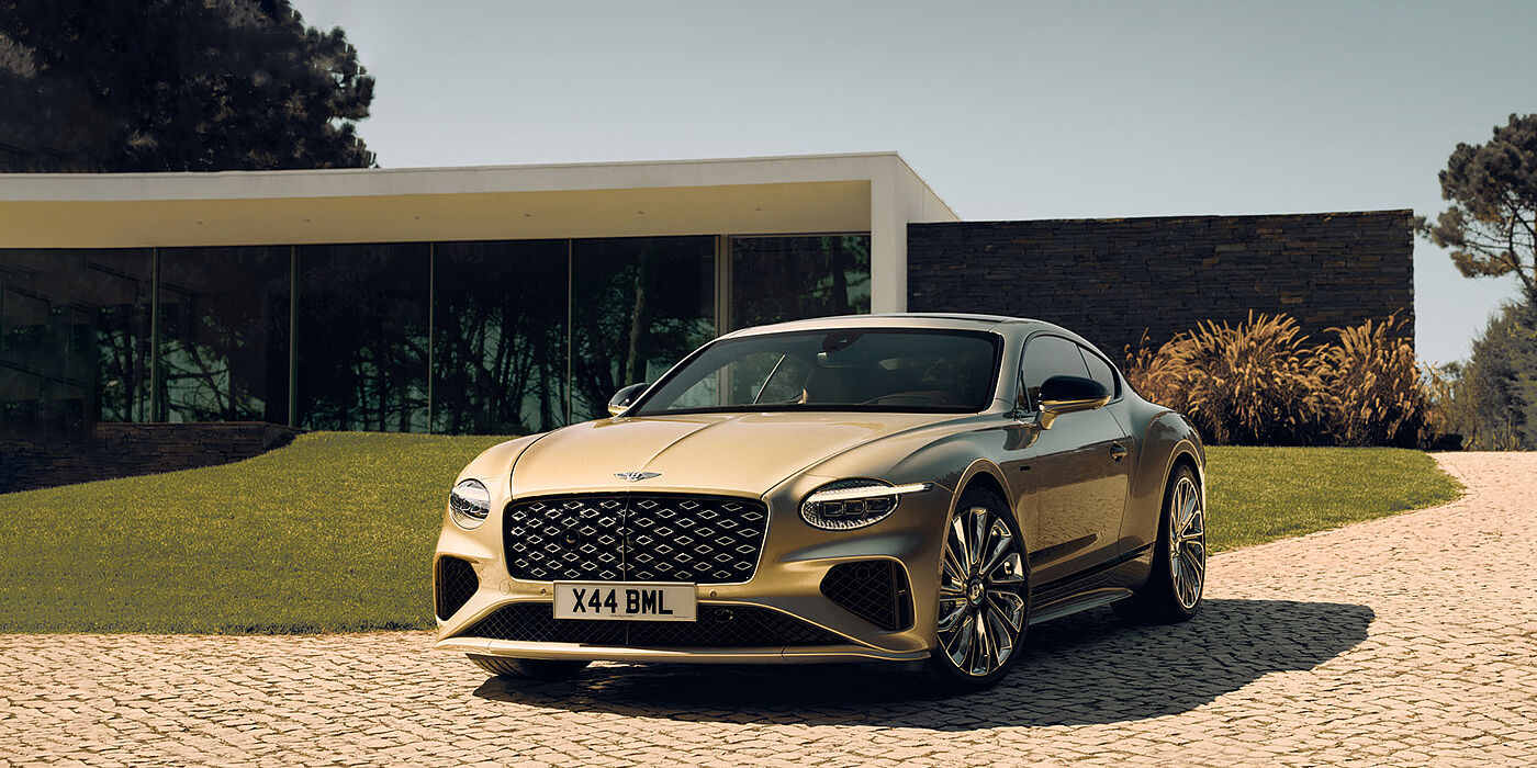 Bentley Ho Chi Minh Bentley Continental GT Mulliner coupe front three quarters in Patina paint parked outside a glass fronted building with a grass lawn behind it