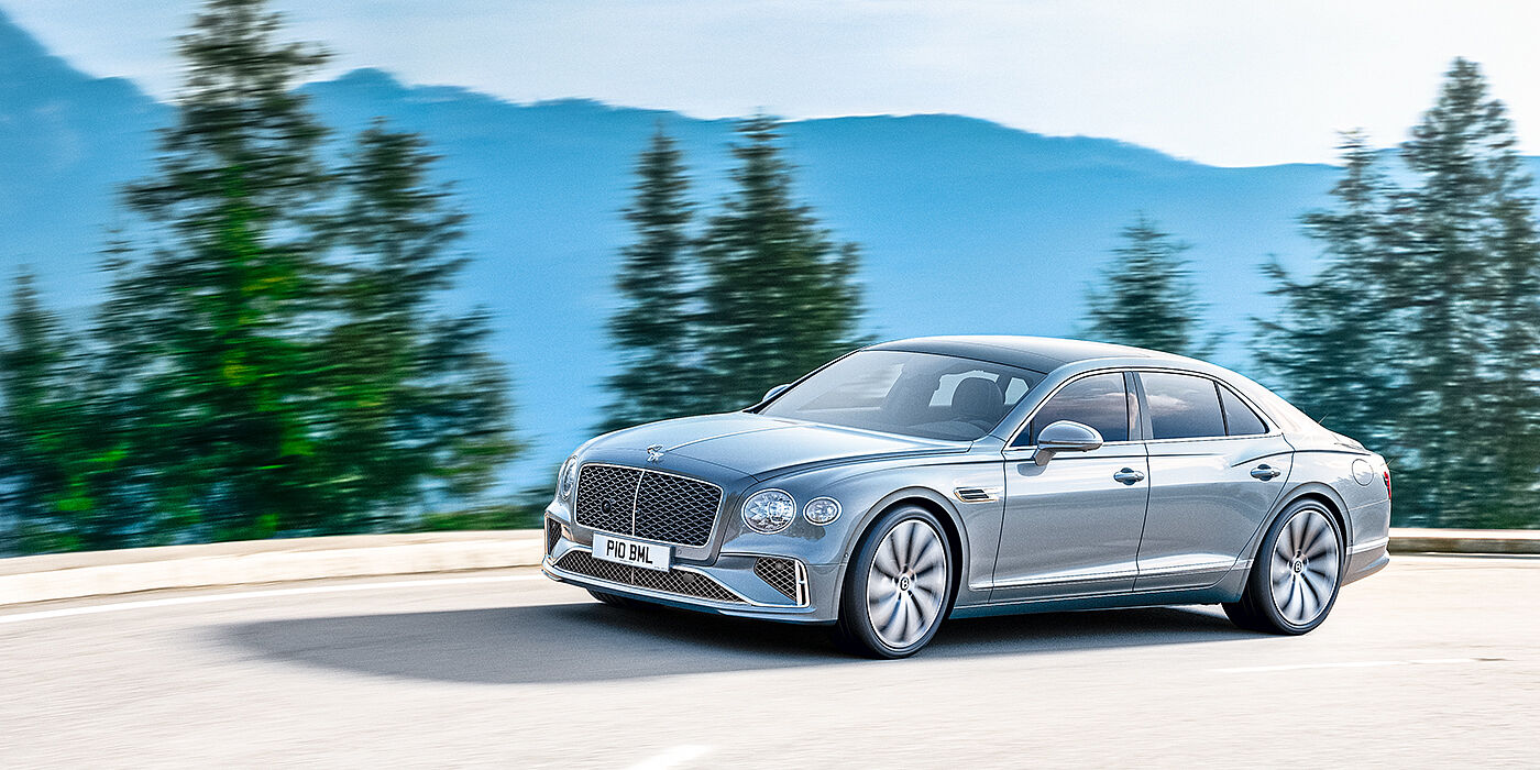 Bentley Ho Chi Minh New Bentley Flying Spur sedan side view in Silverlake paint with ten spoke wheels and chrome matrix grille driving dynamically on a mountain road