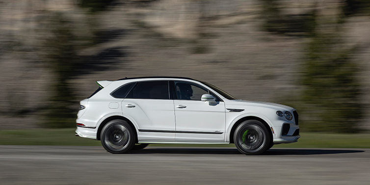 Bentley Bentayga Speed in white is driving on the road with a misty rocky mountain background, the wheels clearly in motion, showcasing the power and luxury of this premium SUV.