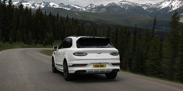 Bentley Bentayga Speed in Glacier White with Hyper Green detailing, driving confidently through a breathtaking mountain landscape – a seamless blend of high-performance power and adventurous spirit.